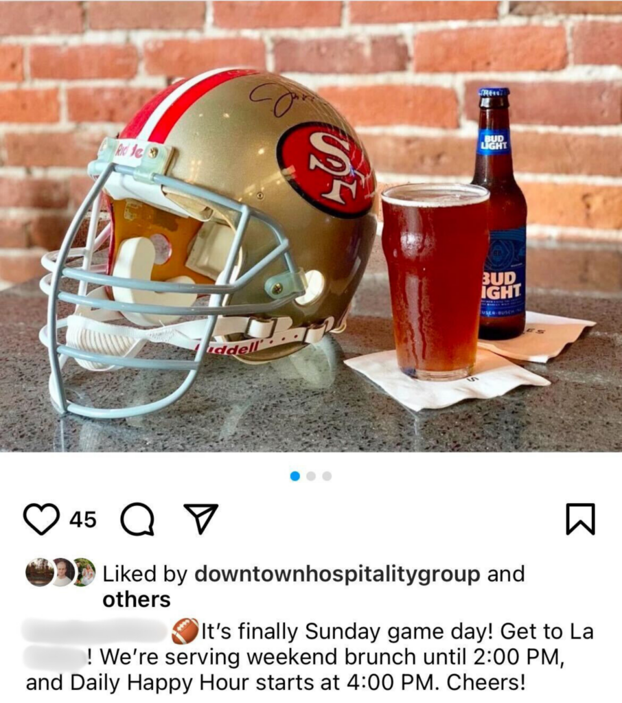 A table with a signed 49ers helmet, a pint of beer, and a bottle of Bud Light at a restaurant, set against a brick wall. The setup exudes game-day excitement and casual dining charm.